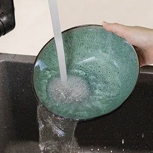 Green ceramic bowl being rinsed under running water in a sink.