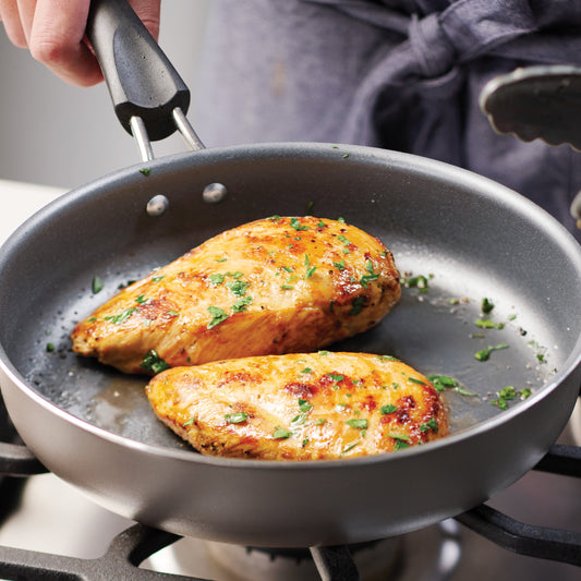 Fried chicken breasts in a pan with herbs, held by a person wearing an apron.
