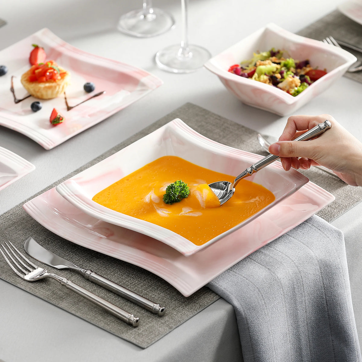 Person eating soup from a white bowl with a silver spoon on a dining table.