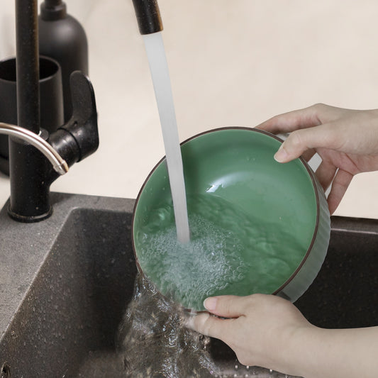 Person washing a green bowl under running water in a kitchen sink.