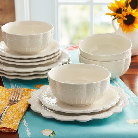 Set of white ceramic dinnerware on a table with a floral placemat and sunflowers.