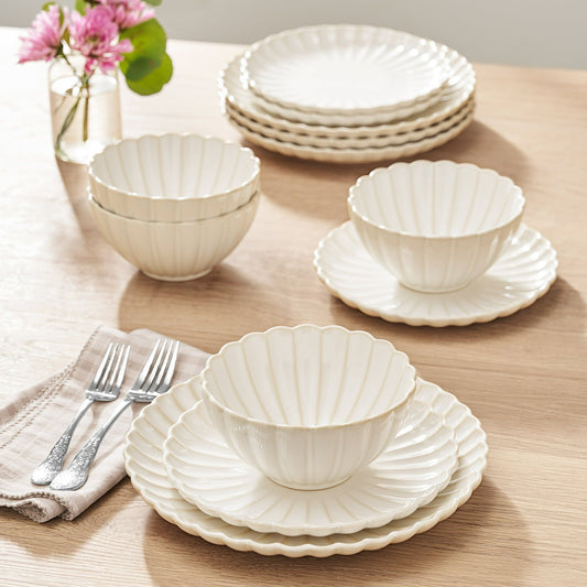 Set of white ceramic dishes including bowls and plates on a wooden table with a vase of pink flowers.