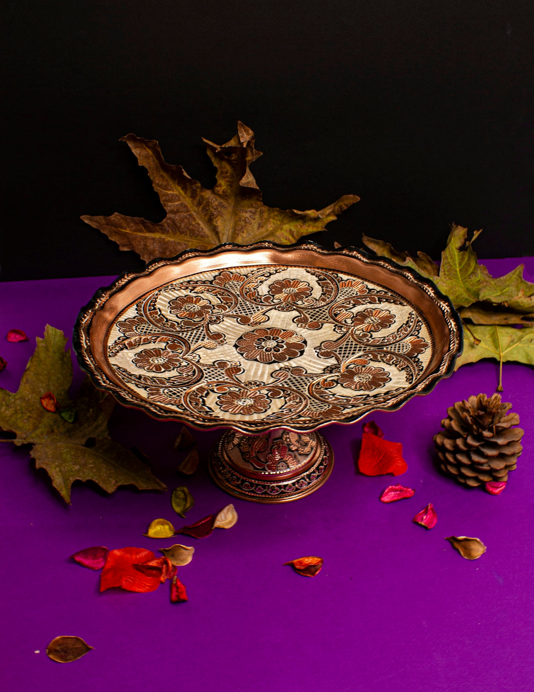a decorative bowl with leaves and a pine cone on a purple surface