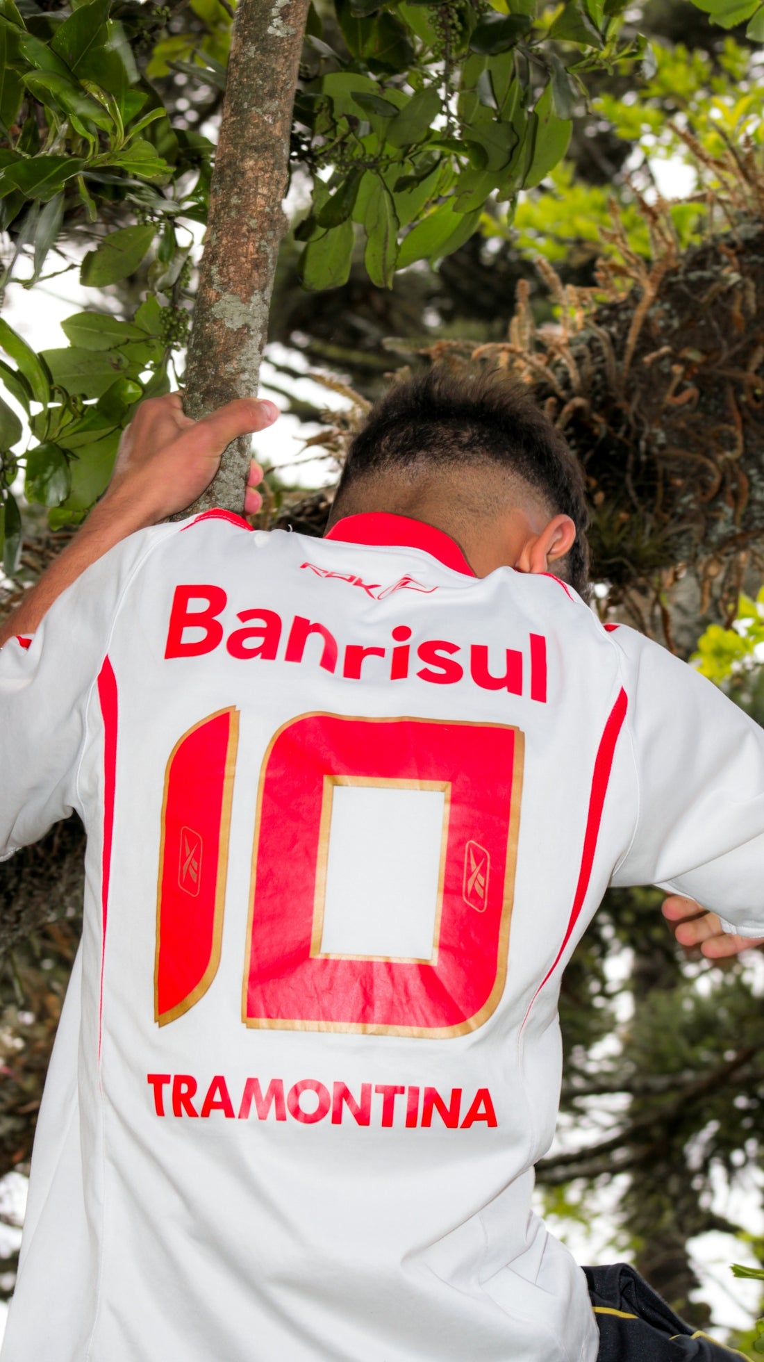 Man in white soccer jersey with red numbers climbing tree