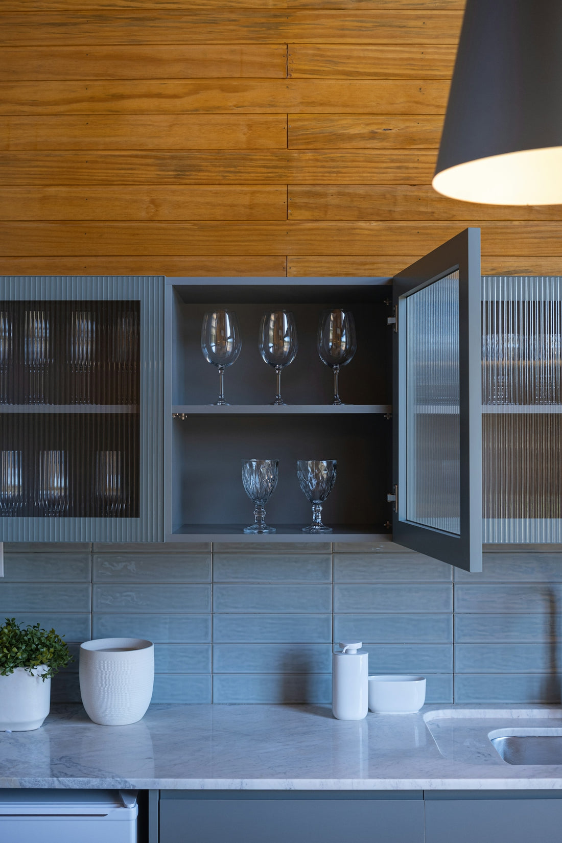 Kitchen cabinets with glassware and wooden wall paneling.