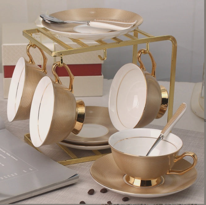 Set of gold and white ceramic tea cups and saucers on a stand with a blurred background.
