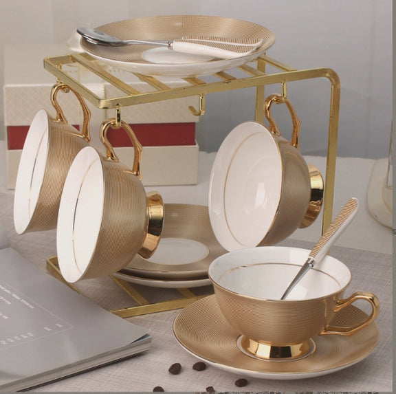 Set of gold and white ceramic tea cups and saucers on a stand with a blurred background.