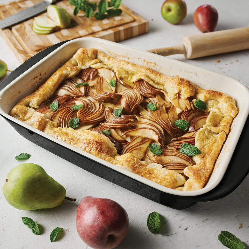 Pear tart in a baking dish with pears and mint leaves on a table