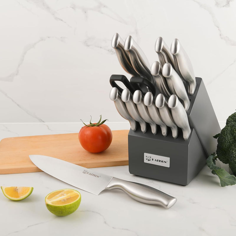 Set of knives in a block with a cutting board, tomato, lime, and broccoli on a white surface.