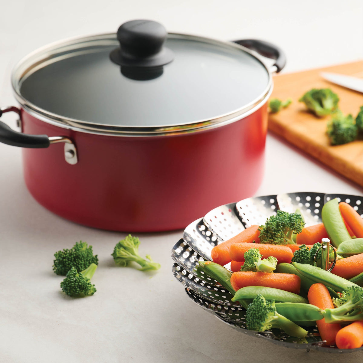 Red pot covered with glass lid and multifunction display accessory with carrots and peas