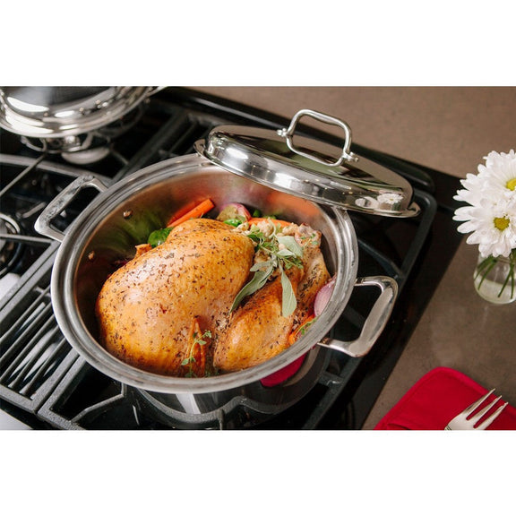 Roasted chicken in a pot on a stove with a decorative flower arrangement in the background.