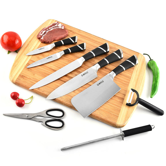 Set of knives with black handles on a wooden cutting board, surrounded by vegetables and scissors.