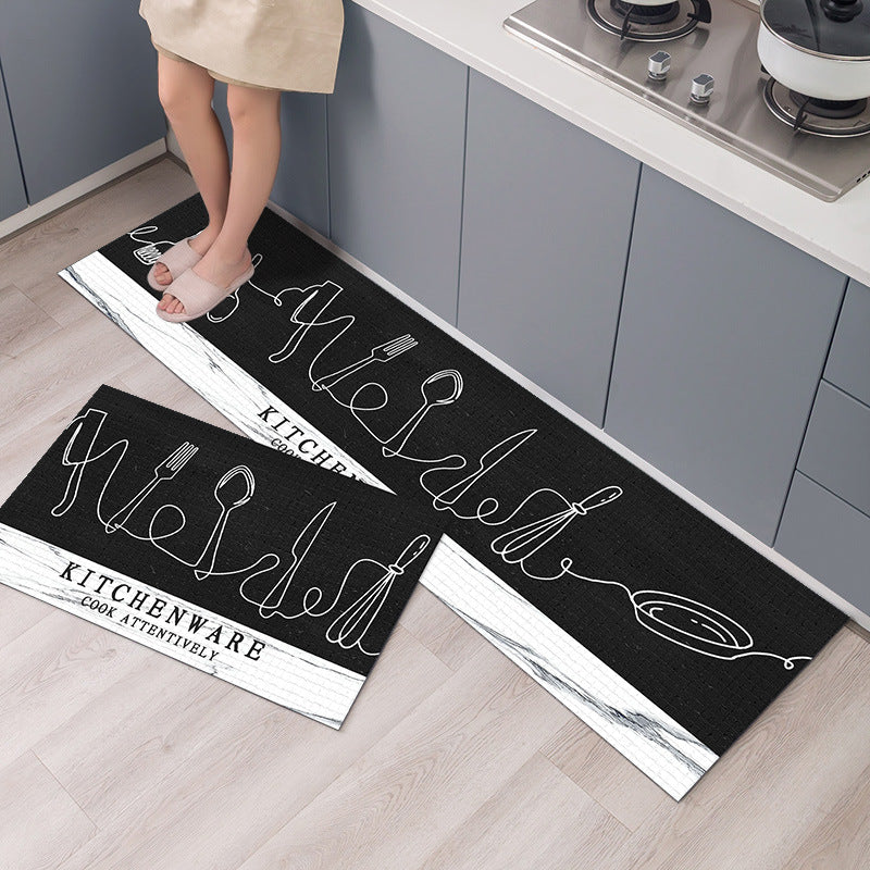 Two black kitchen mats with white text and graphics on a wooden floor.