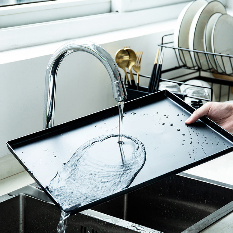 Person washing a baking tray under running water in a kitchen sink.