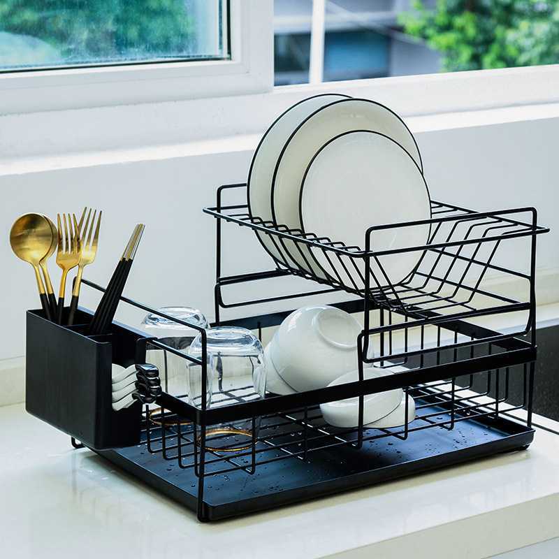 Black dish rack with white plates and gold utensils on a kitchen counter.