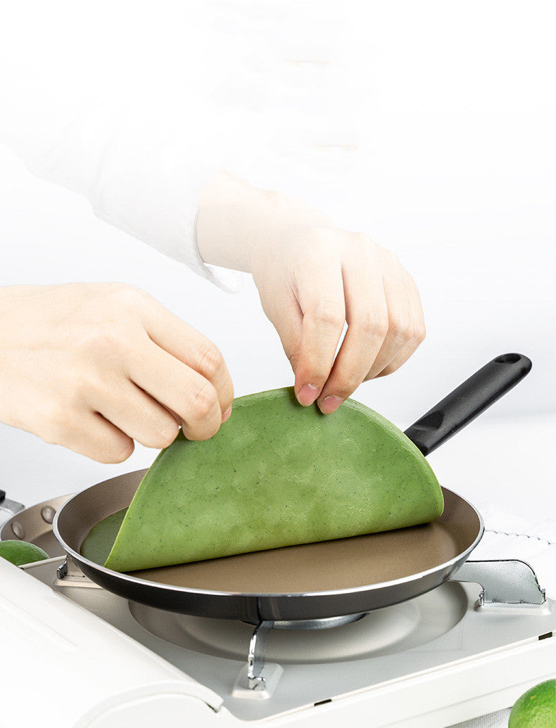 Person making a green wrap on a frying pan with a white background