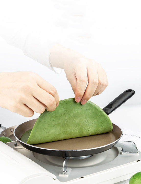 Person making a green wrap on a frying pan with a white background