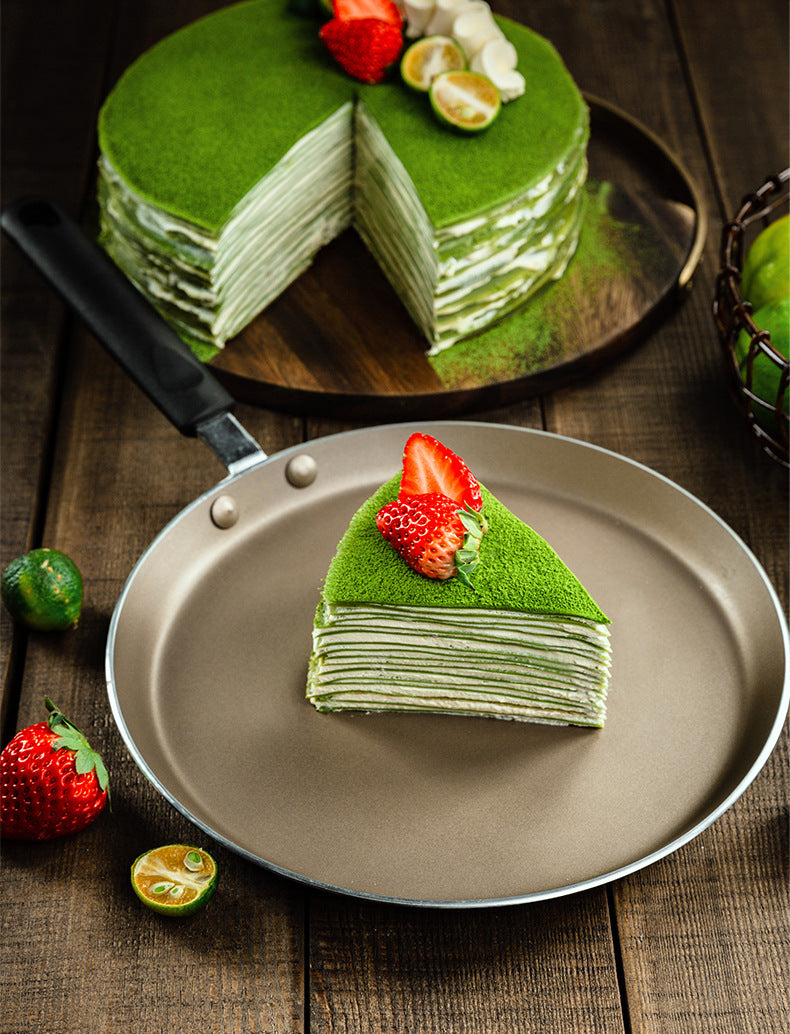 Green layered cake with a slice on a plate, surrounded by strawberries and limes on a wooden table.
