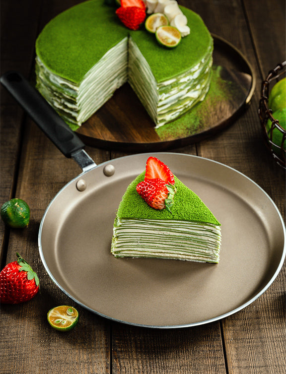 Green layered cake with a slice on a plate, surrounded by strawberries and limes on a wooden table.