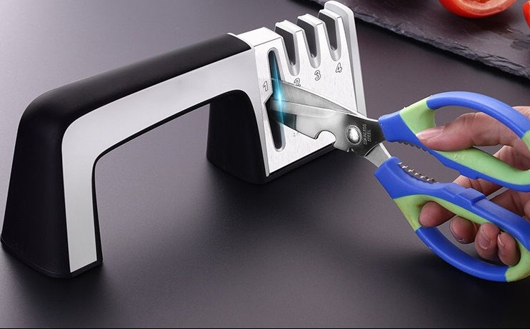 Scissor sharpener with a pair of blue-handled scissors being sharpened on a dark surface.