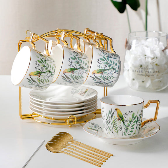 Ceramic tea set with floral design on a white surface, featuring cups, saucers, and a gold stand.