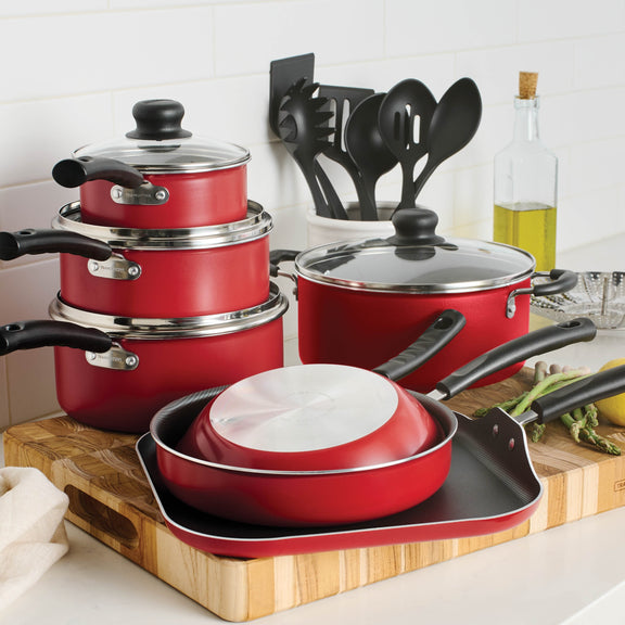 Red cookware set covered with glass lids sitting on cutting board with vegetable oil in bottle