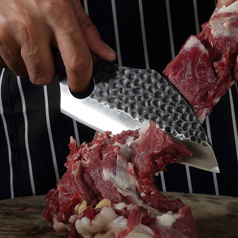 Person cutting raw meat with a knife on a wooden surface