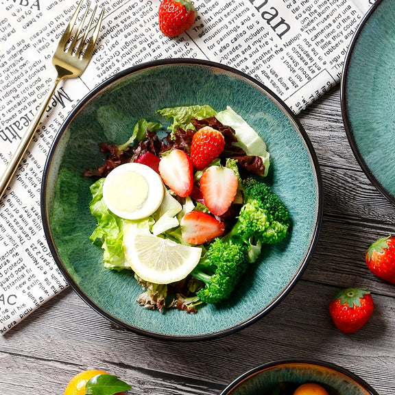 Green salad with strawberries and lemon slices on a blue plate, placed on a newspaper.