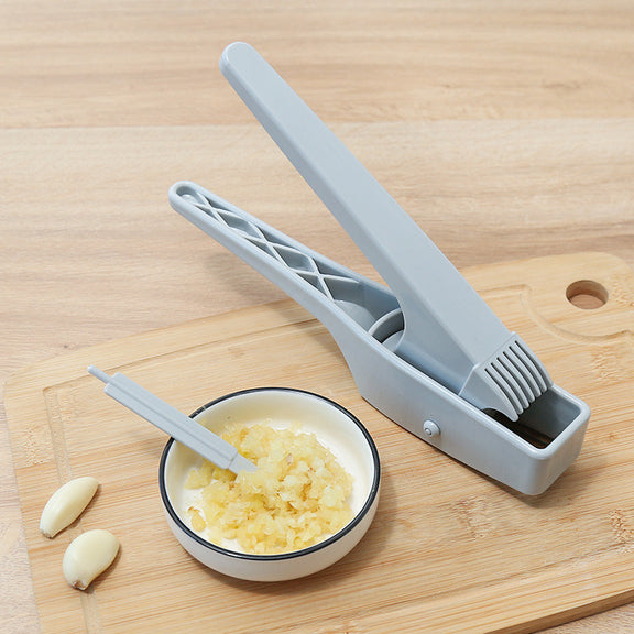 Gray garlic press on a wooden cutting board with minced garlic in a bowl and whole garlic cloves.