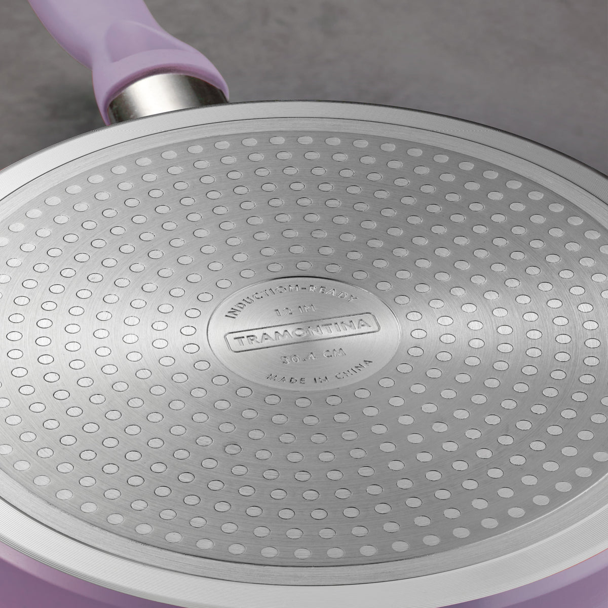 Close-up of a Tramontina frying pan with purple handle on a gray background