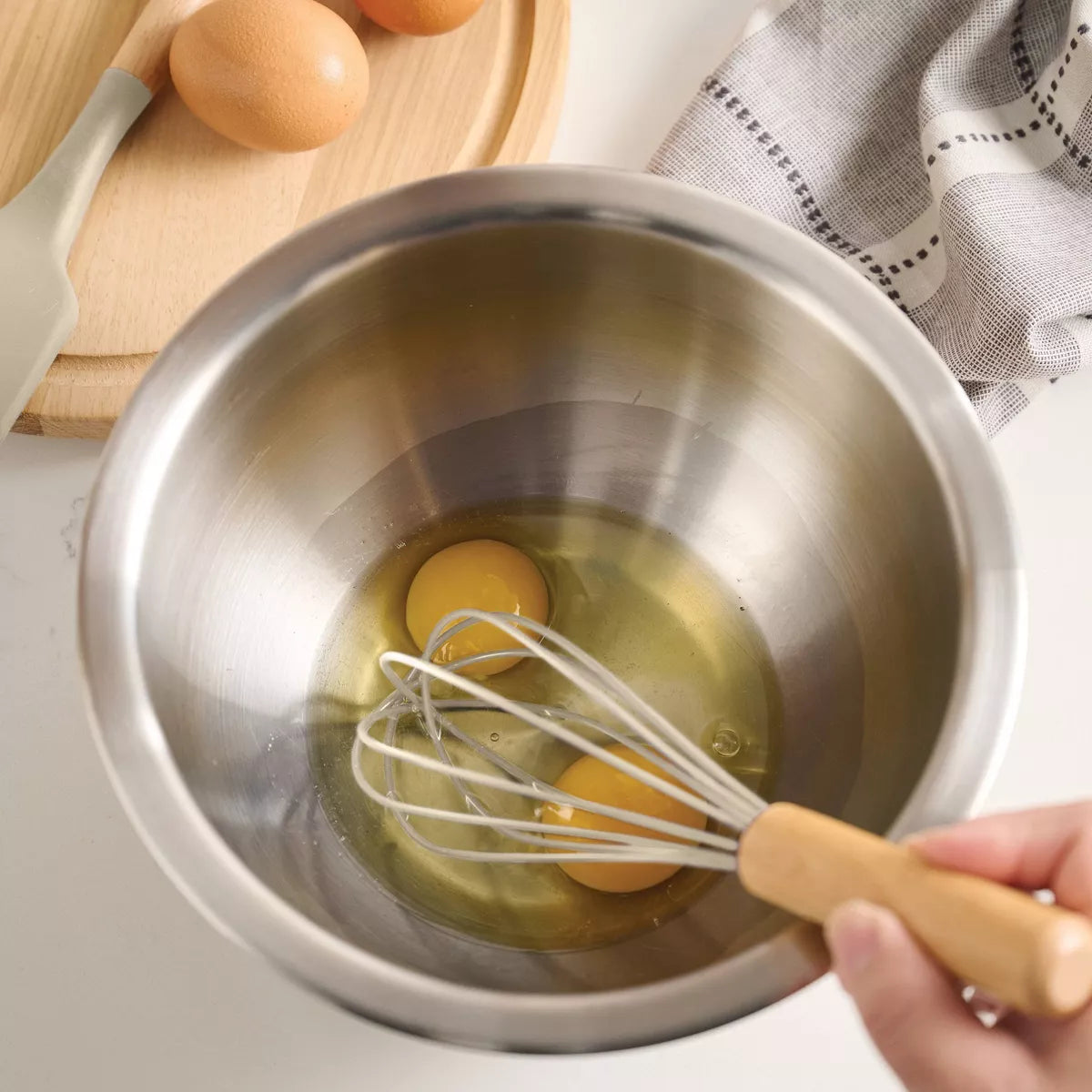 Eggs being whisked in a metal bowl with a hand holding the whisk.
