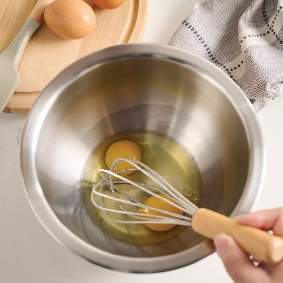 Eggs being whisked in a metal bowl with a hand holding the whisk.