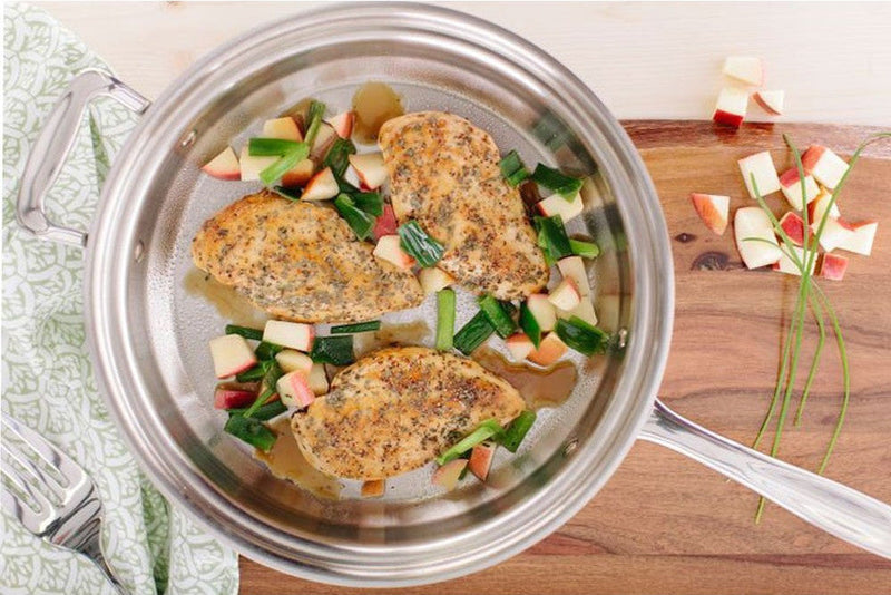 Stir-fried chicken with vegetables in a stainless steel pan on a wooden surface.