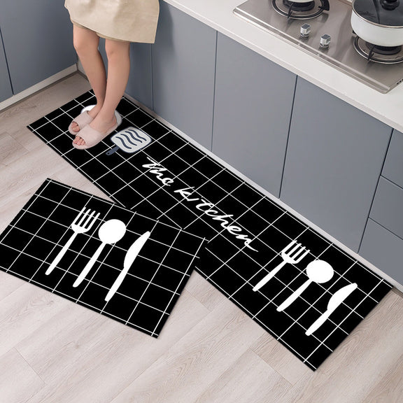 Two black kitchen mats with white utensil designs and 'The Kitchen' text on a wooden floor.
