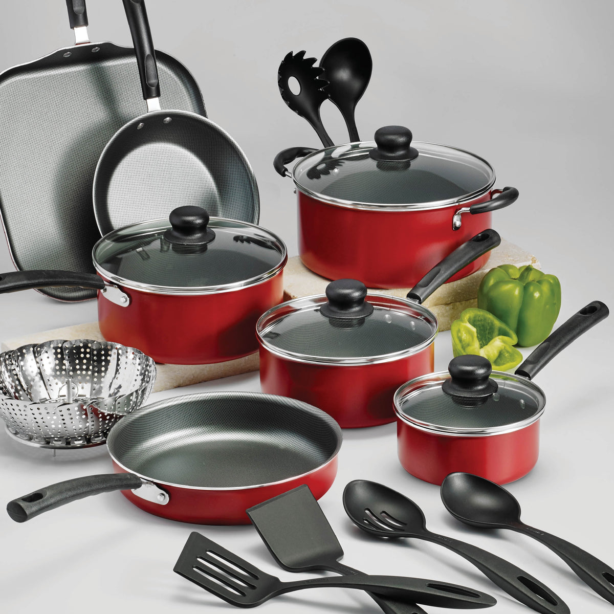 Picture of red cookware set with kitchen utensils and glass lids on grey background