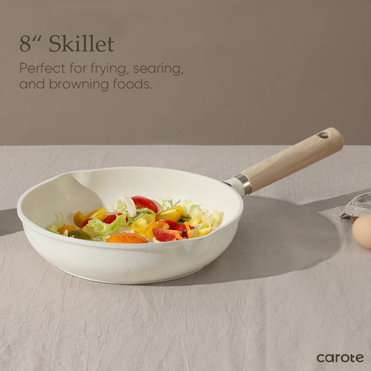 White skillet with wooden handle containing vegetables on a neutral background, featuring text about its use.