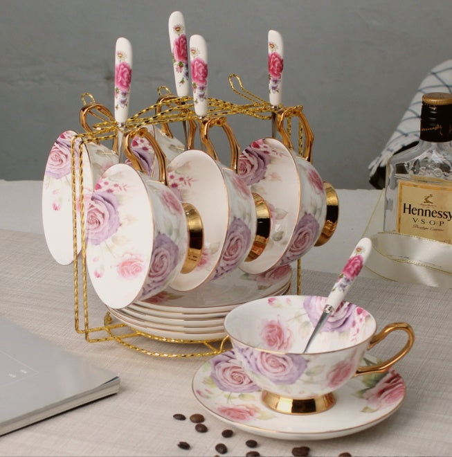 Set of floral teacups and saucers with spoons on a stand, Hennessy VSOP bottle in the background.