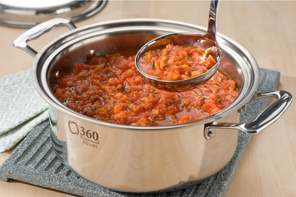 Stainless steel pot with tomato sauce and a ladle on a wooden surface
