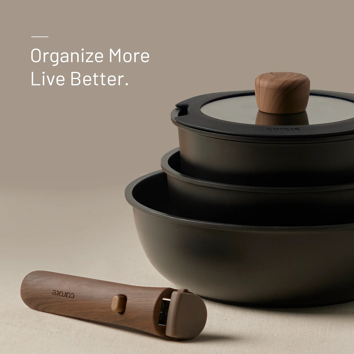 Set of black pots with glass lids and wooden handles on a beige background, featuring the brand 'Carote.'