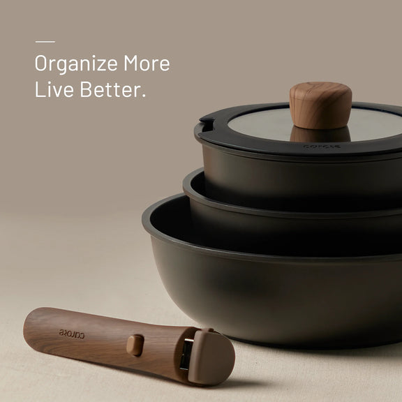 Set of black pots with glass lids and wooden handles on a beige background, featuring the brand 'Carote.'