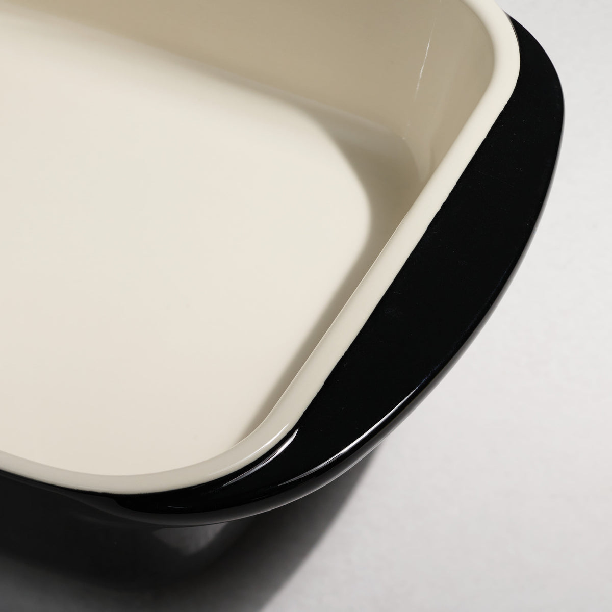 Two square ceramic dishes, one beige and one black, on a light gray background.