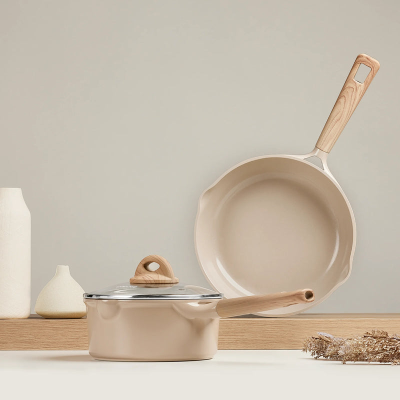 Beige cookware set with wooden handles on a neutral background