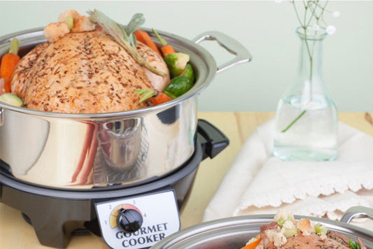 Gourmet cooker with a roasted chicken and vegetables on a table.