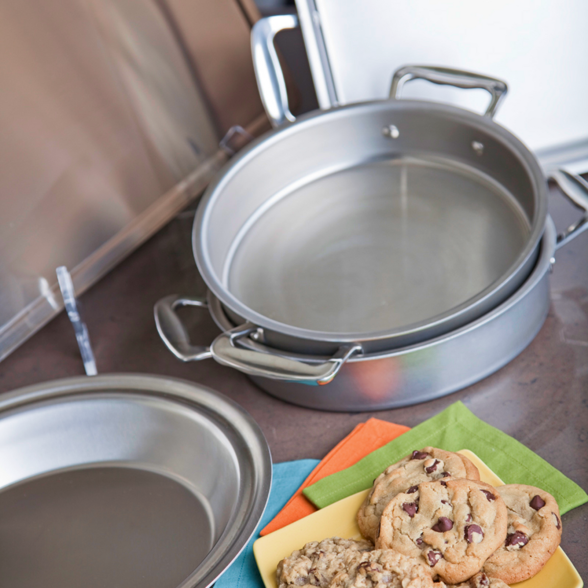Metal baking pans on a kitchen counter with cookies on a plate.