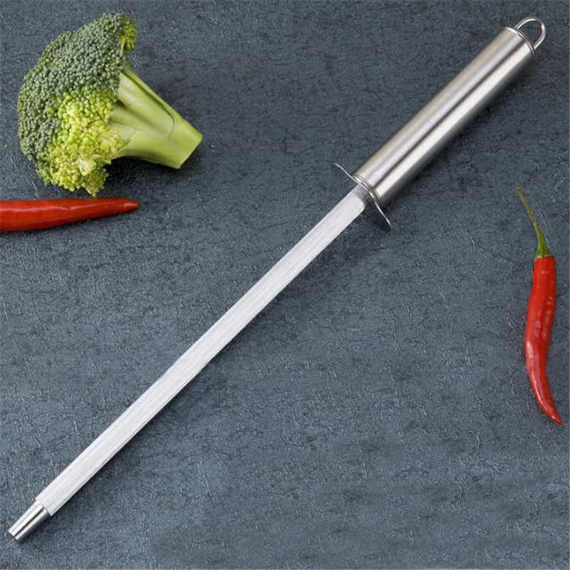 Metal knife on a dark surface with broccoli and red chili peppers.
