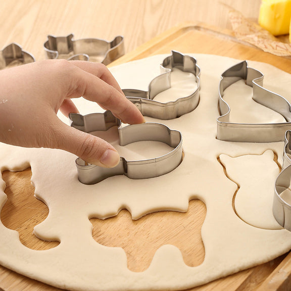 Hand using a metal cookie cutter on rolled-out dough with various animal shapes.