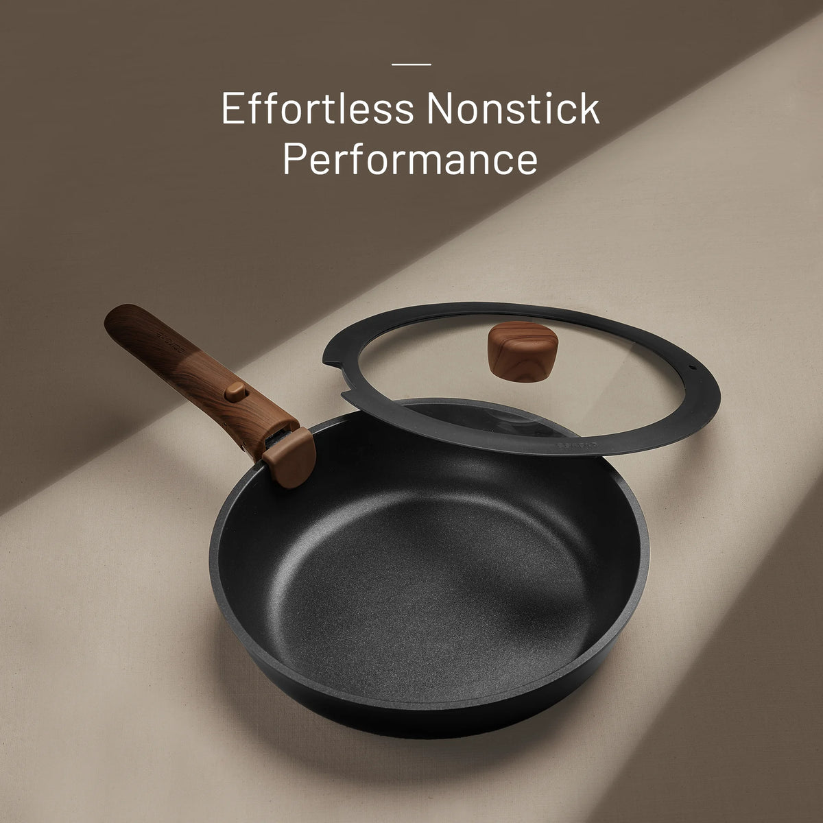Black frying pan with wooden handle and glass lid on a beige surface, featuring text 'Effortless Nonstick Performance'.