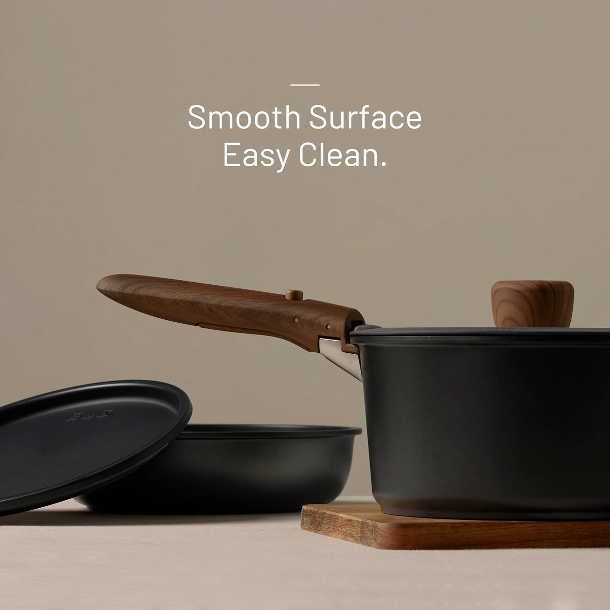 Black cookware set with wooden handles on a beige background, featuring text 'Smooth Surface Easy Clean.'