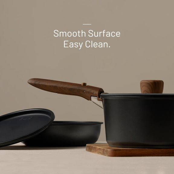 Black cookware set with wooden handles on a beige background, featuring text 'Smooth Surface Easy Clean.'