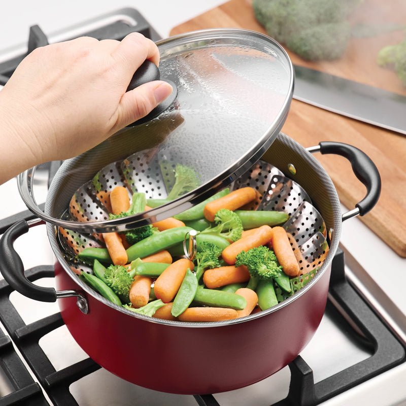 Hand hold glass lid over red pot with multifunction cooking accessory with carrots and peas on stove